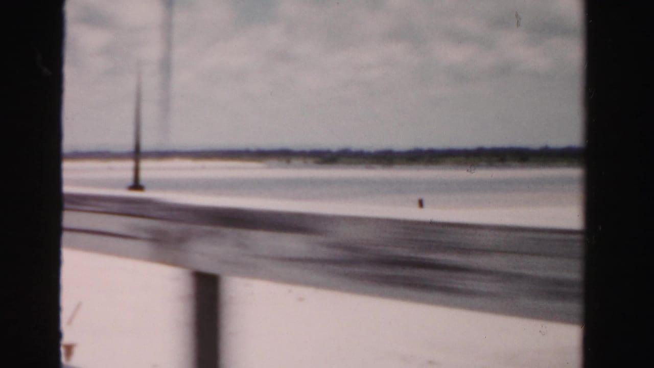 Bridge rail beside open water with a tall lamppost and distant shoreline in soft focus.