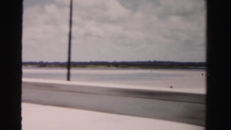 1955 Dade County, Florida 8mm frame showing a lamppost, bridge barrier, open water, and far shoreline.