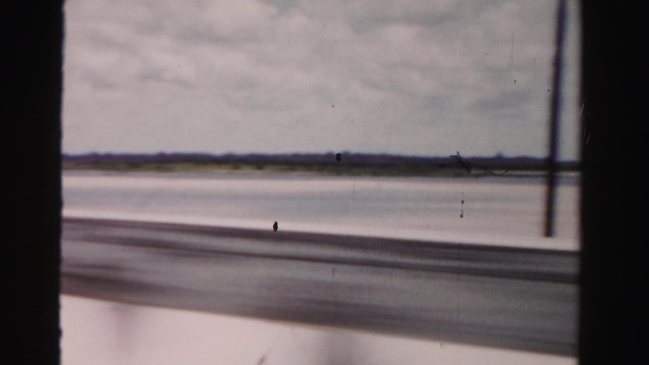 Blurred bridge-side view over water and sand with a lamppost near the right edge and dark framing.