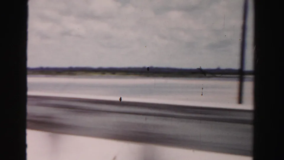 Moving 8mm view in Dade County, Florida, showing flat coastal water and sand through dark vehicle or bridge framing.