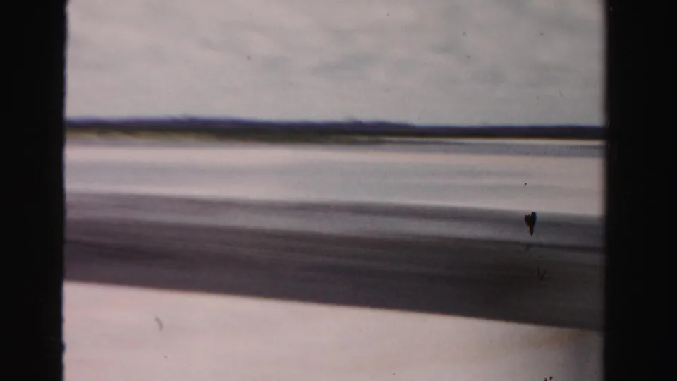 Dade County, Florida 8mm frame showing a low coastal horizon, water, sand, and dark framing during vehicle travel.