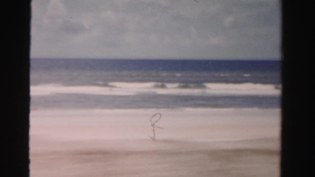 Low waves break near a pale sandy shoreline with dark vertical film borders.
