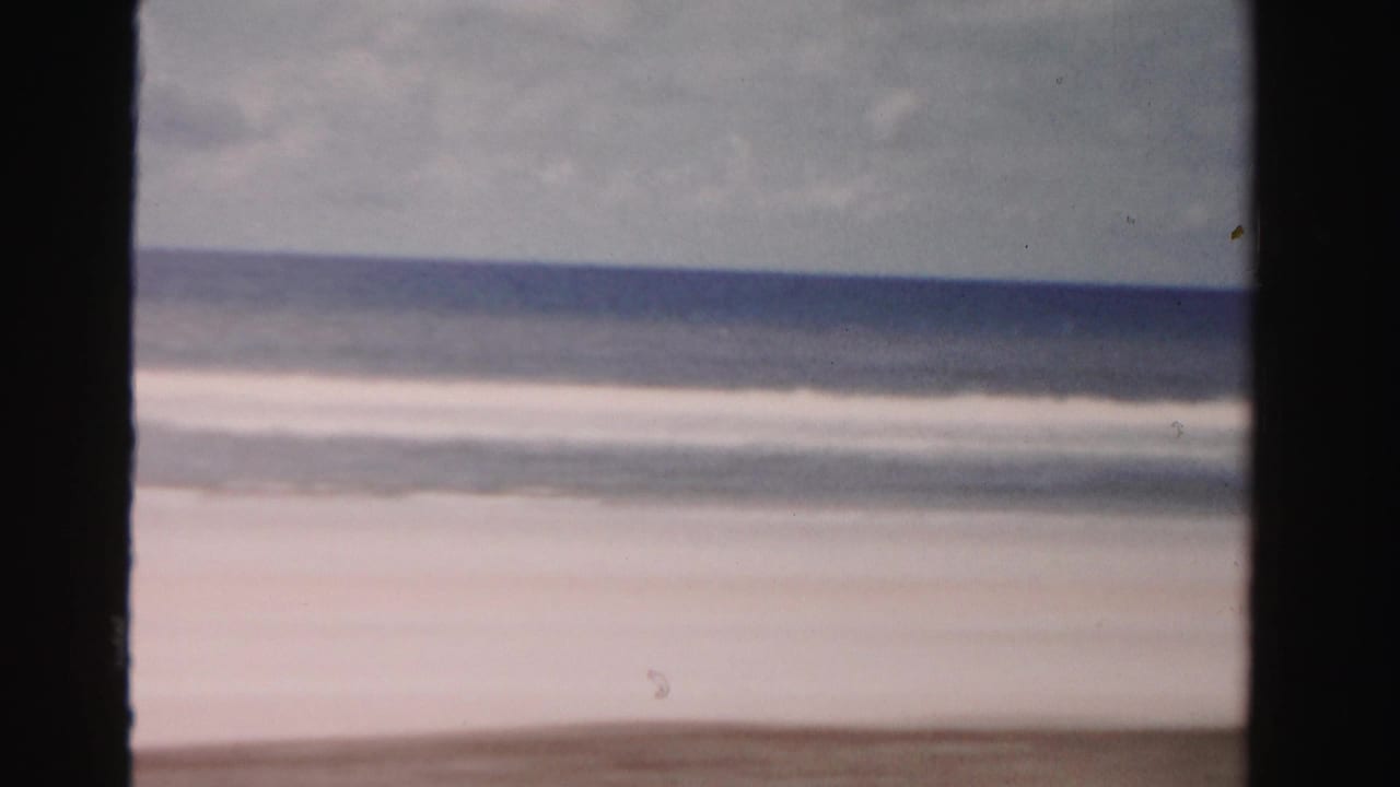 1955 Dade County, Florida beach view from a moving car, with surf, horizon, and dark window-like borders.