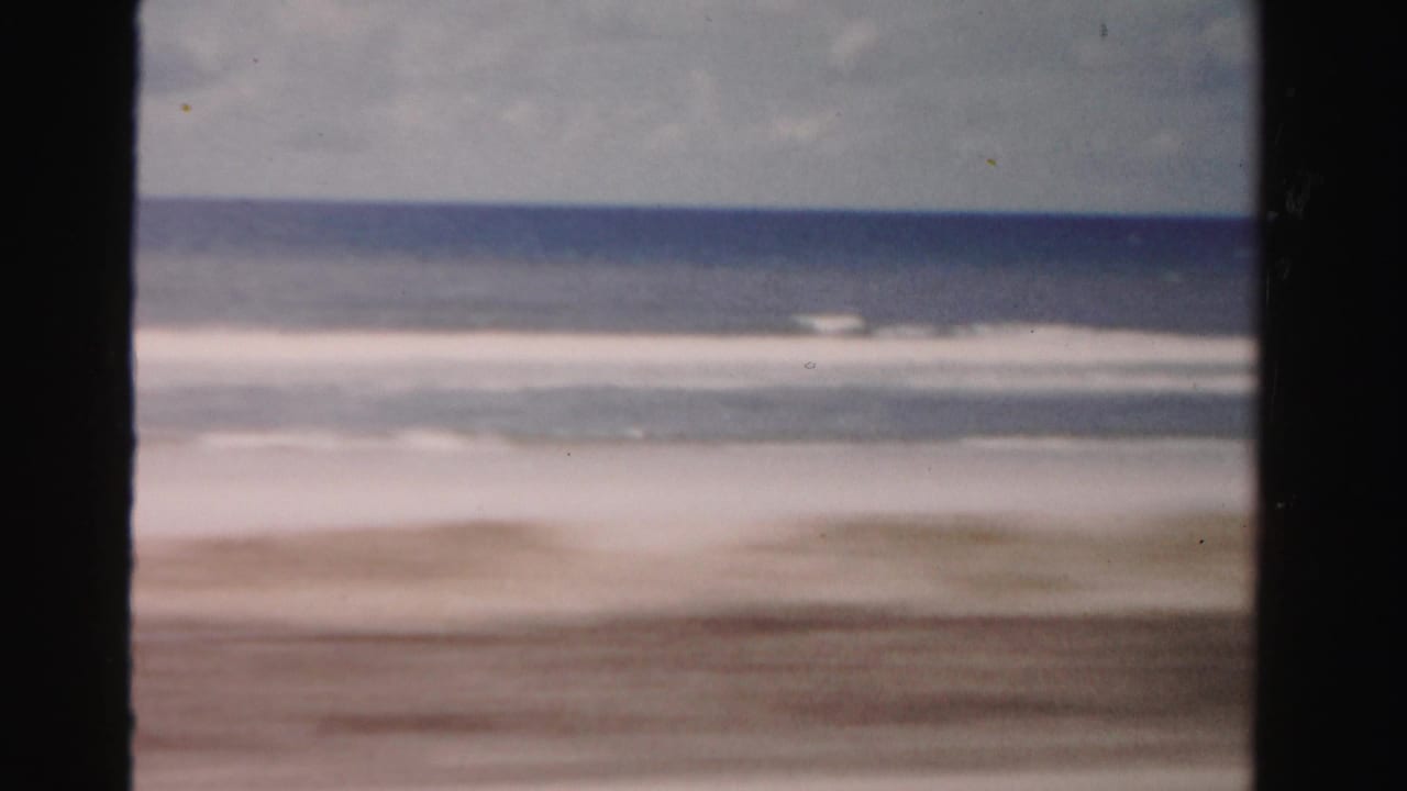 Mid-century 8mm view of Dade County shoreline, with surf bands and a dark foreground divider from the moving vantage point.