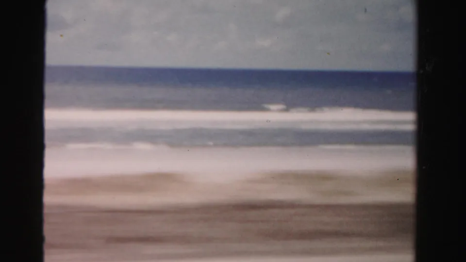 Mid-century 8mm view of Dade County shoreline, with surf bands and a dark foreground divider from the moving vantage point.