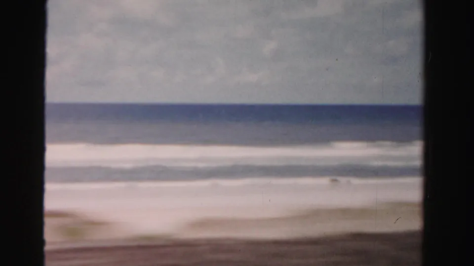 1955 Florida coastal home-movie frame showing waves, beach, and overcast sky from a passing car viewpoint.
