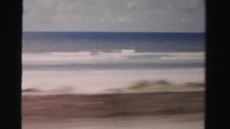 Dade County beach scene from 1955 metadata, showing surf, horizon, muted sky, and foreground blur from a moving car.
