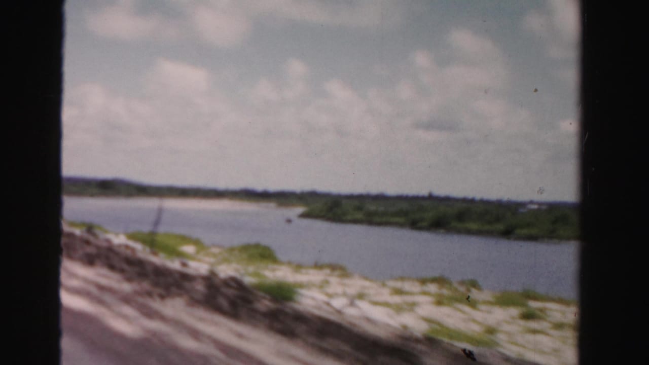 Waterway beside a blurred roadside with green banks and cloudy sky.