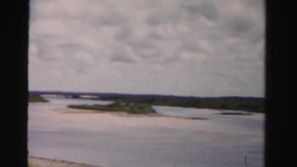 1955 Dade County, Florida 8mm view of open water, small green landforms, pale shoreline areas, and a hazy clouded sky.
