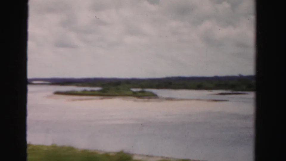 1955 Dade County, Florida home-movie frame showing a waterway, low island-like banks, green vegetation, and soft 8mm exposure.