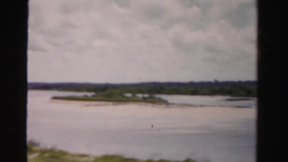1955 Dade County, Florida home-movie frame showing water, low distant greenery, cloudy sky, and dark 8mm frame borders.