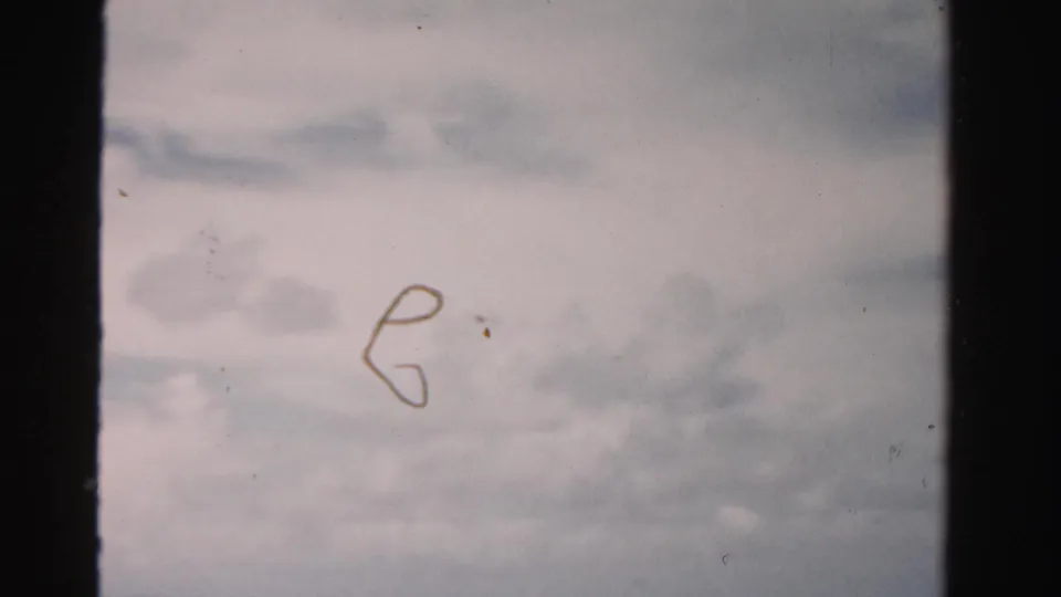 The 8mm frame shows cloudy sky over the coastal setting, with visible dust and soft exposure from the home-movie scan.