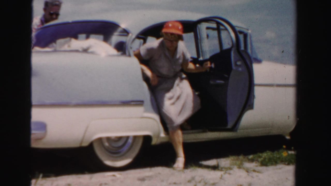 Woman in a red hat steps out of a blue and white sedan with the door open.