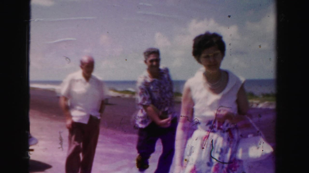 Three adults walk toward the camera on a coastal road with ocean and sky behind them.