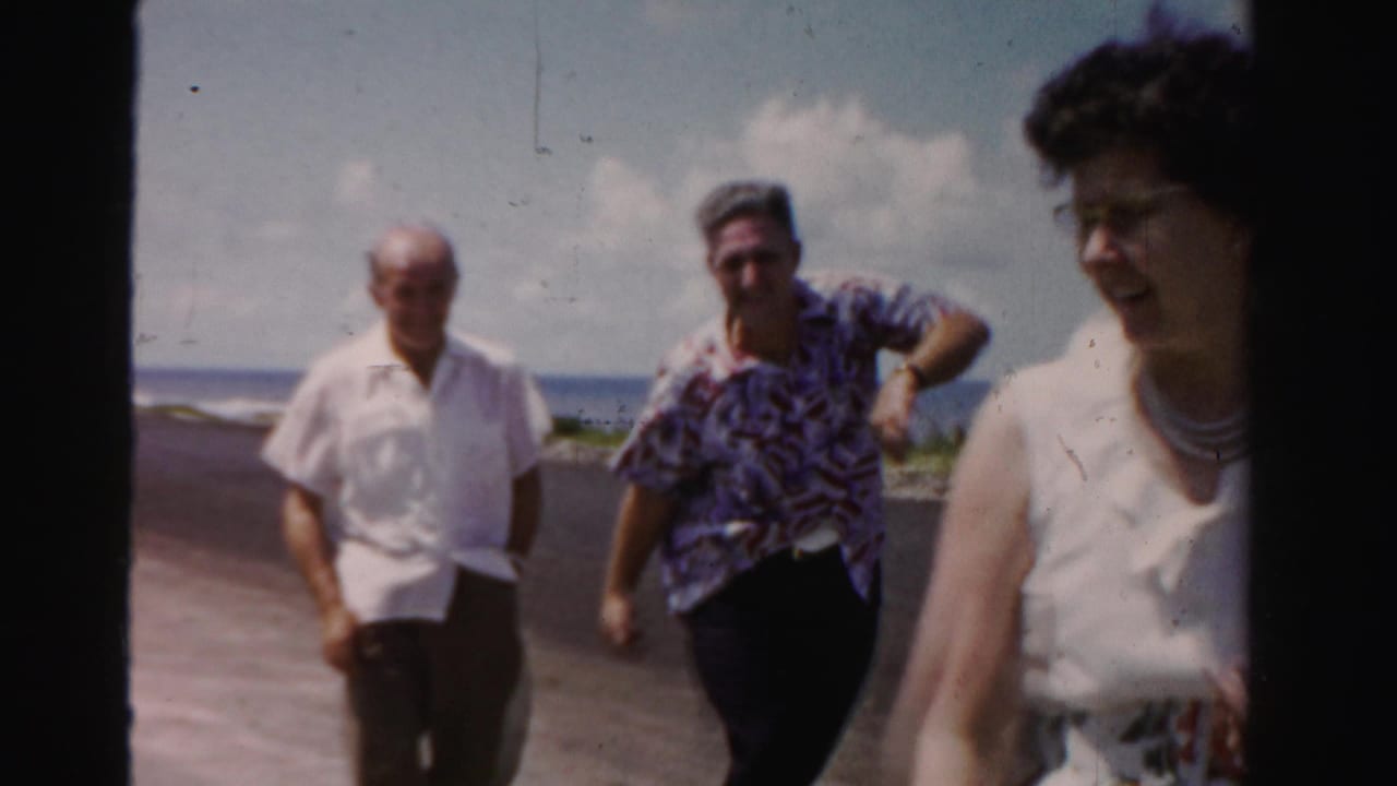 Three adults continue walking along the road, with a woman near the right edge of the frame.