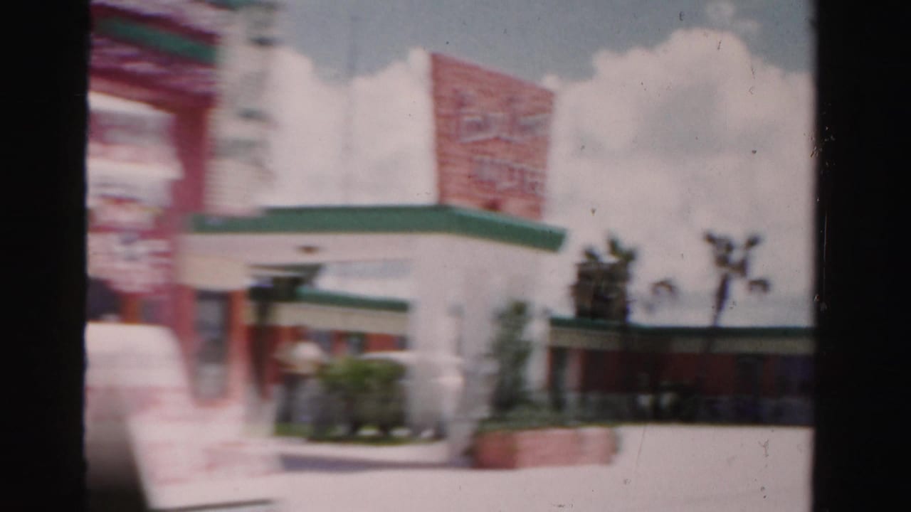 Blurred roadside view of a white building with a red sign and green roof trim.