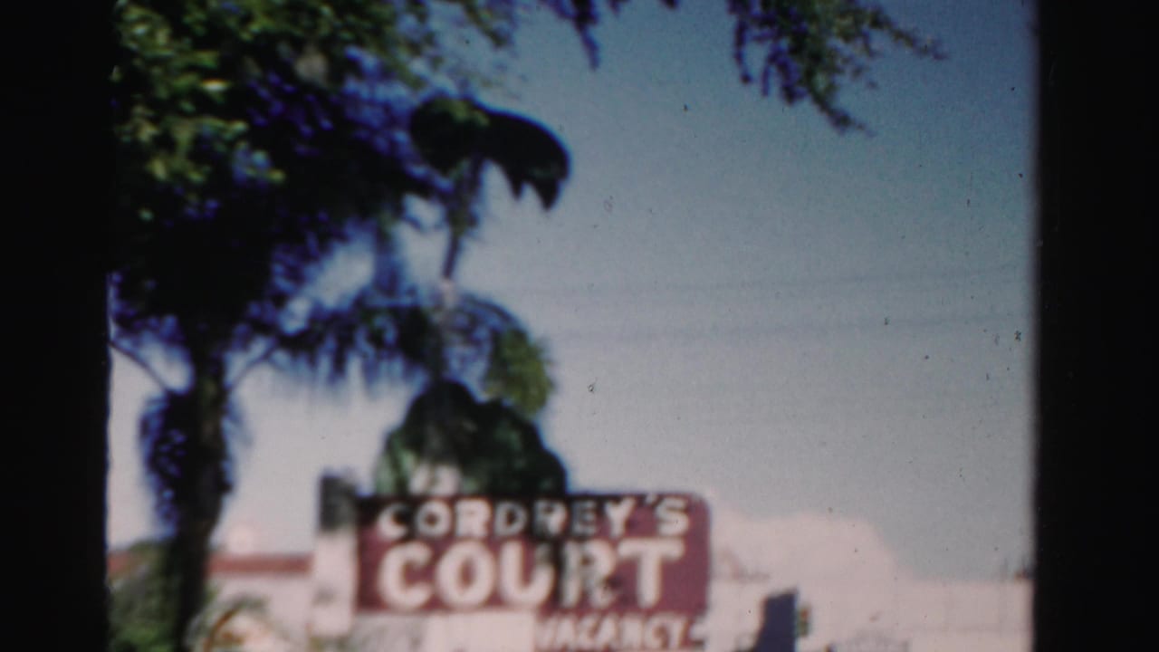 1955 Dade County home-movie frame showing the Cordrey's Court vacancy sign beneath palm trees along a roadside.