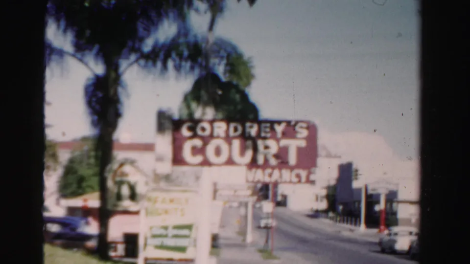 1955 Dade County roadside view of the Cordrey's Court vacancy sign with palm trees, modest buildings, and cars along the street.