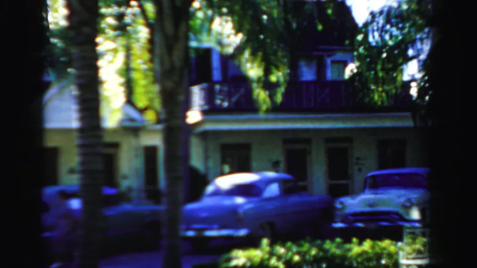 1955 Dade County home-movie view of a two-story house or court building, palm trunks, and parked cars along the street.