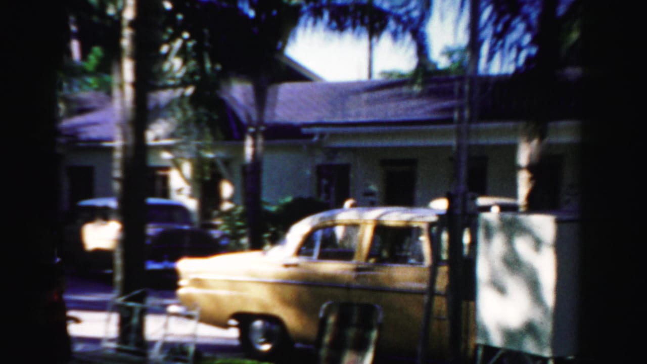 Parked yellow car in front of a stucco building with palm trees and deep shade.