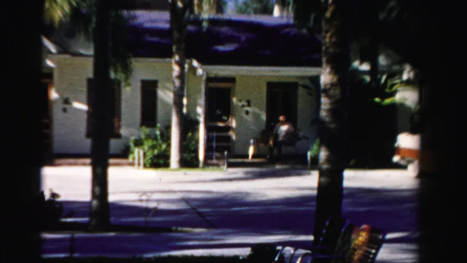 Final 8mm frame shows the figure low near the front entrance of the Dade County house, partially obscured by shadow and distance.