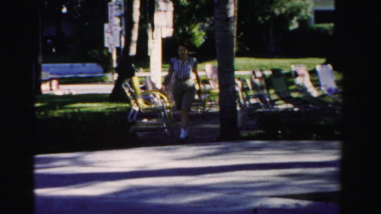 Woman walking near palm trees and lounge chairs on a shaded resort path.