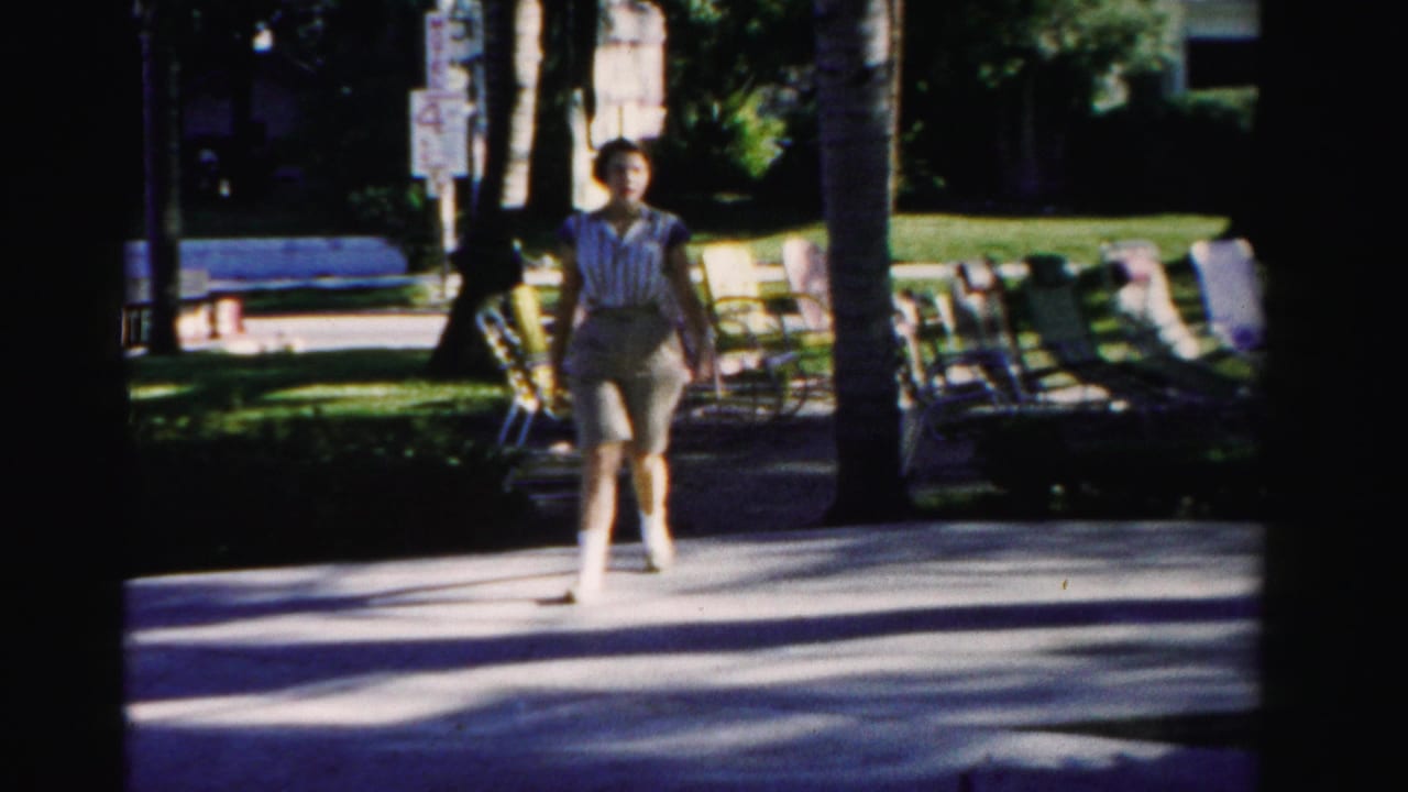 Woman in shorts walking toward the camera on a palm-lined resort walkway.