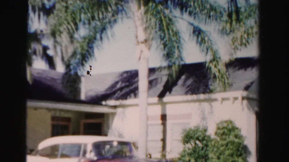 Final 8mm frame holds on the Dade County residence with palms, bushes, dark roof, and a cropped light-colored car in front.