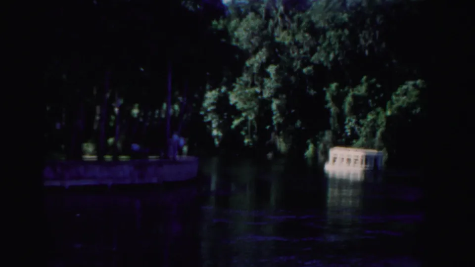 Shaded Dade County waterway with dense trees, a shoreline structure, and a small white boat or ferry at right.