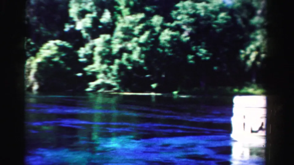 A larger white passenger boat partly enters the 1955 Dade County frame, close to the camera on a wooded waterway.