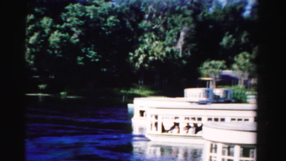 Large white passenger boat passes near the camera on a Dade County waterway, with seated people visible through the side openings.