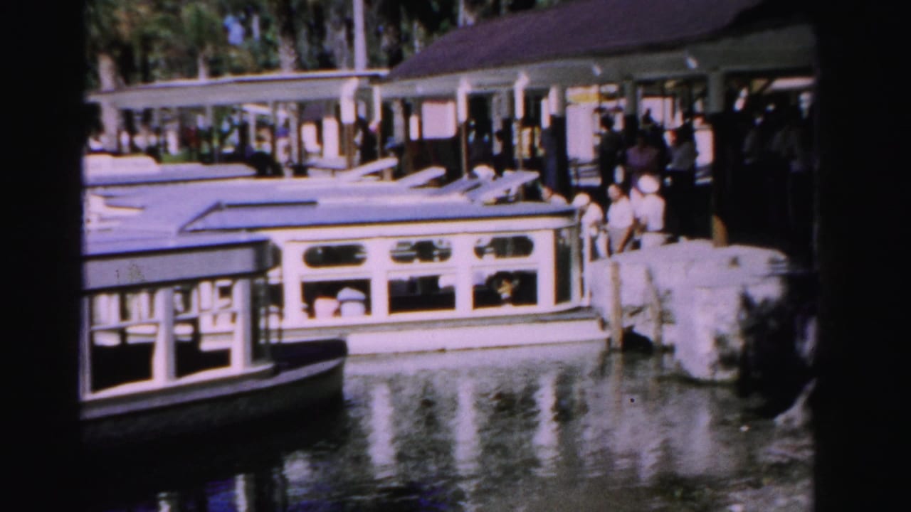 1955 Dade County waterfront view with people on a covered pier beside a white open-sided passenger boat.