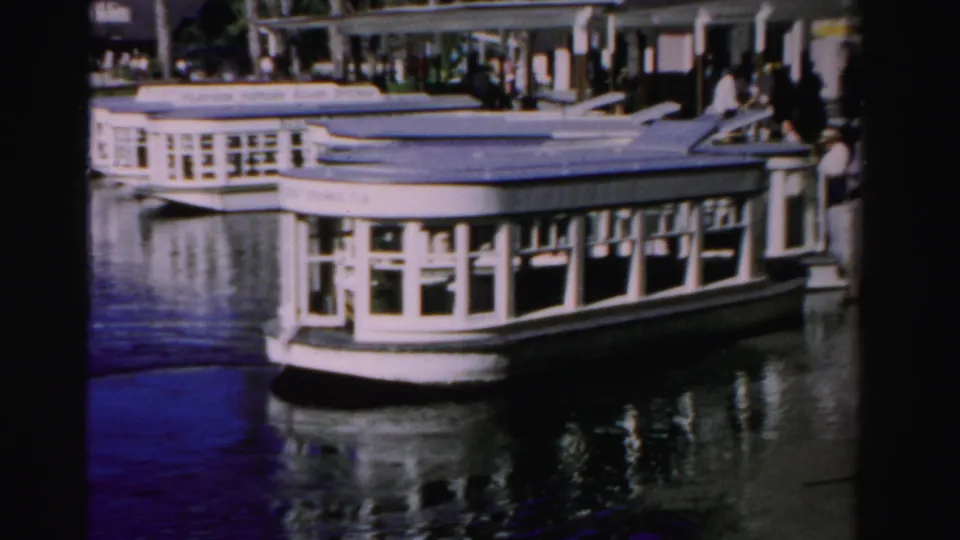 Broadside view of a white passenger boat at a sunny Dade County pier, with people visible under the covered dock.