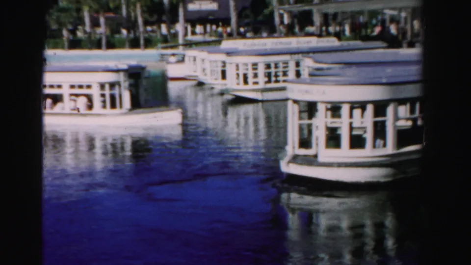 White passenger boat beside a Dade County waterfront, with palm trees, windows, and reflections visible in the water.