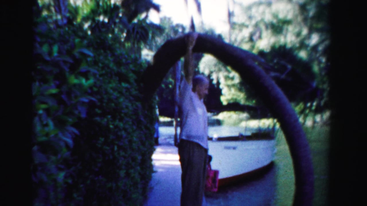 Man reaching upward to touch a curved tree branch beside a white boat.