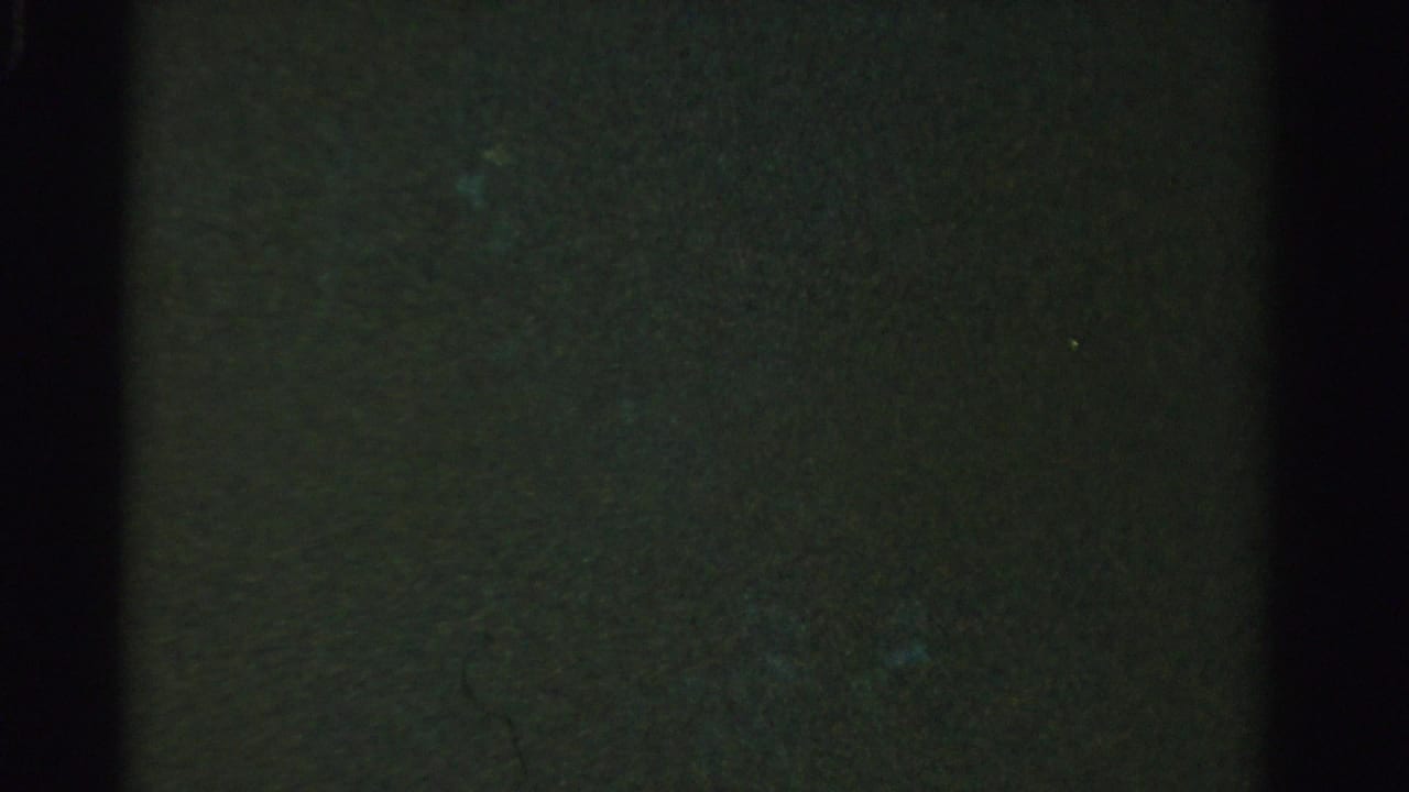 Mostly dark green-black frame with heavy grain and faint light variation.