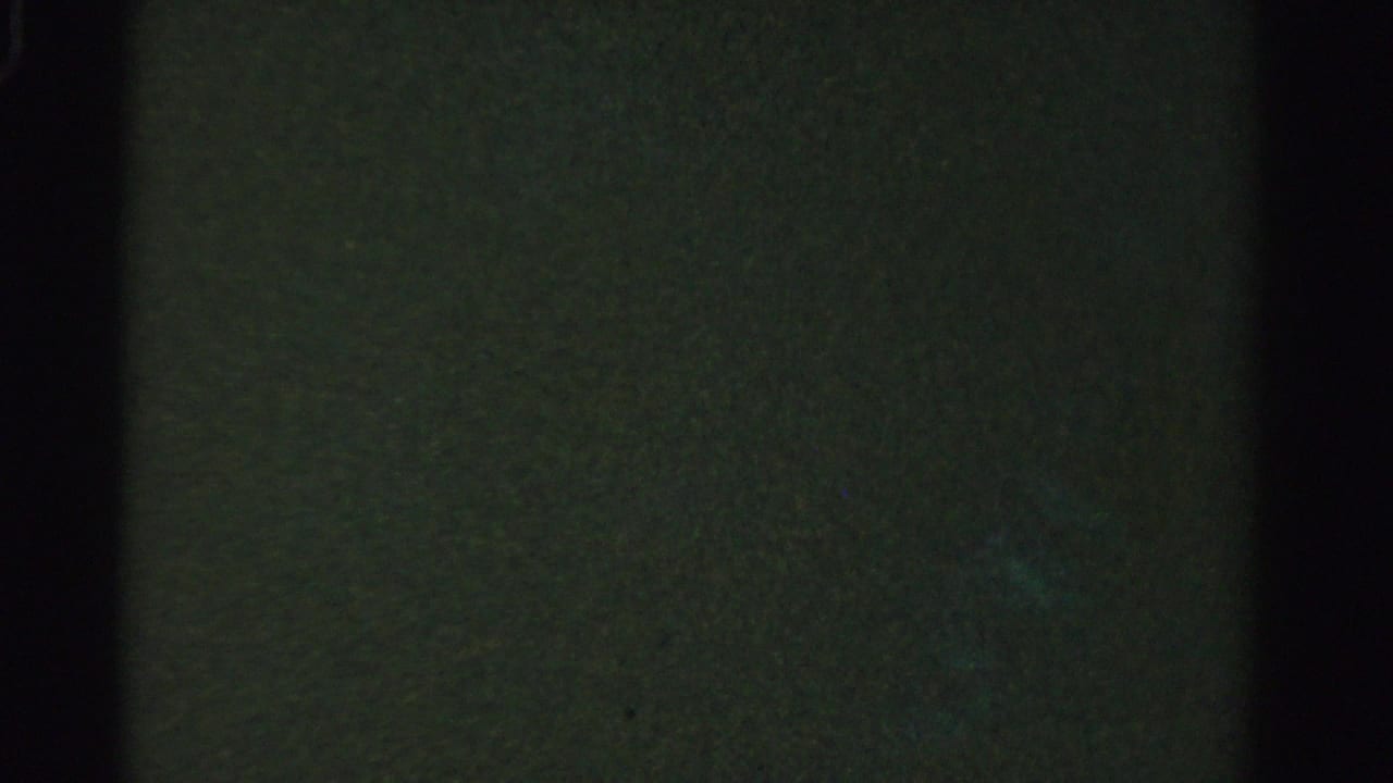 Dark, mostly indistinct underwater frame with faint green-blue texture and black film edge.