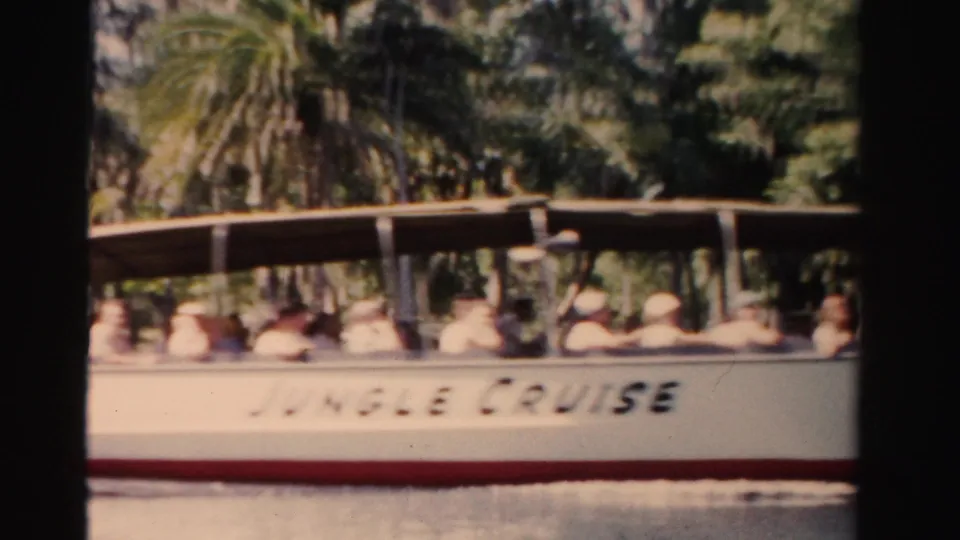 Passengers sit aboard an open white tour boat with JUNGLE CRUISE lettering during a 1950s Florida river-tour scene.
