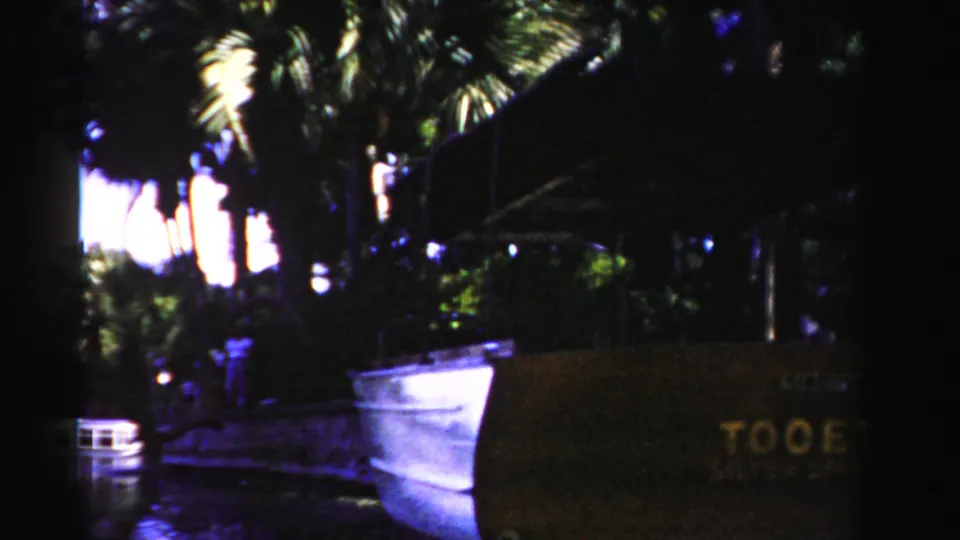 1955 Dade County waterfront frame with a white boat near the dock, palm trees behind it, and the brown TOOETWO sign at right.