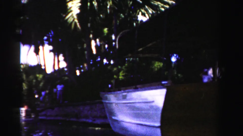 1955 Dade County 8mm frame showing a white boat near a palm-lined waterfront, with part of the foreground sign cropped at right.