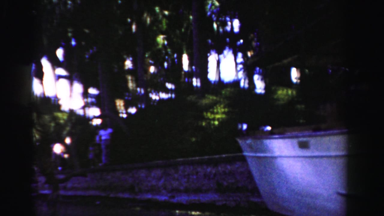 1955 Dade County riverside view with a pale boat under heavy tree shade and a person partly visible near the bank.