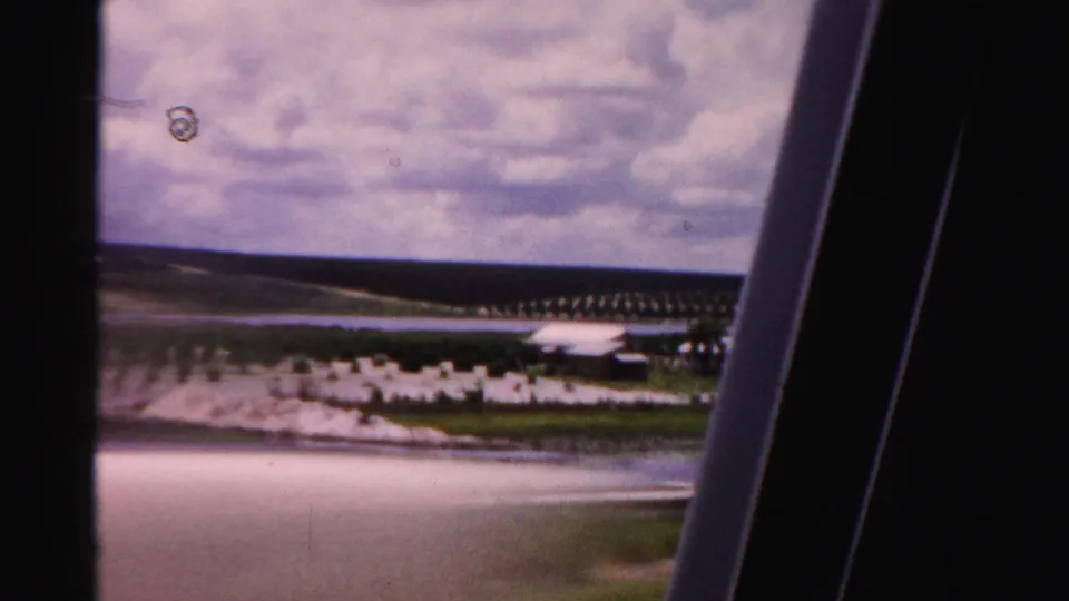 Moving 8mm view of Dade County agricultural land with rows of trees, water, and low pale structures.