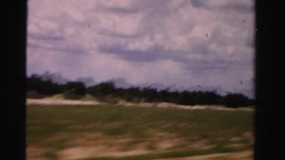 1955 Dade County road-trip footage showing open grassland, distant trees, cloudy sky, and dark 8mm frame borders.