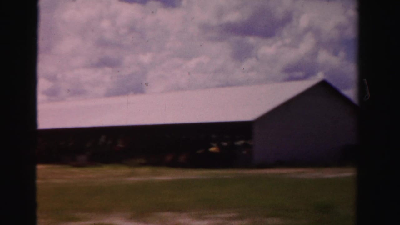A long rural building appears beside open ground in Dade County, Florida, filmed in soft, faded 1950s 8mm color.