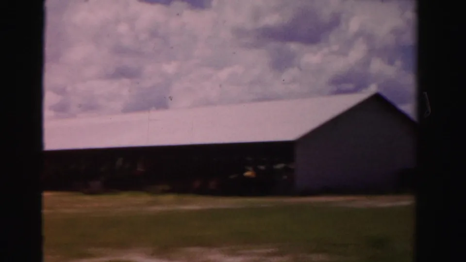 A long rural building appears beside open ground in Dade County, Florida, filmed in soft, faded 1950s 8mm color.