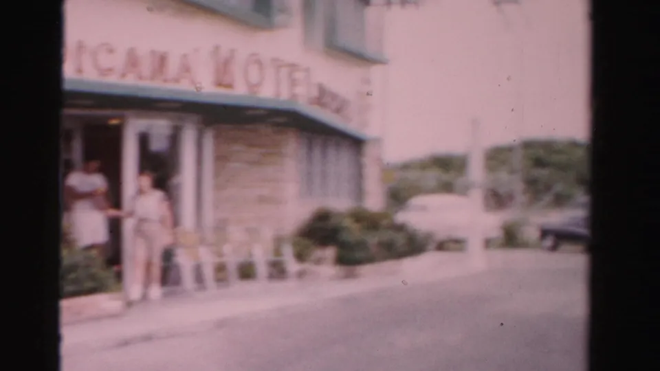 1955 Dade County motel frontage showing two adults at the entrance under Tropicana Motel signage and parked cars beyond.