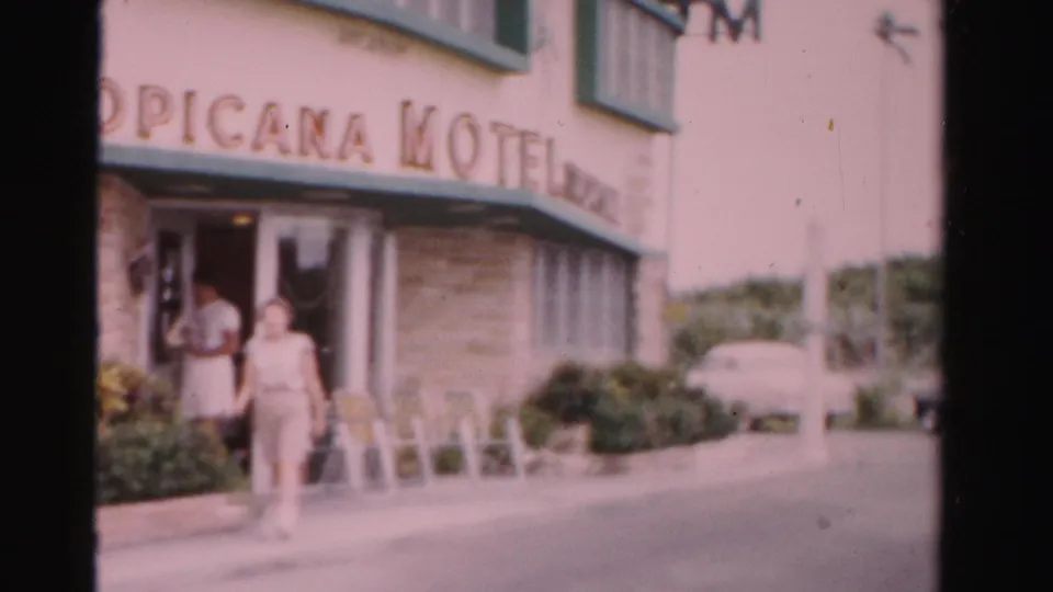 1955 Dade County, Florida motel sidewalk with a woman walking past the entrance and Tropicana Motel sign above.