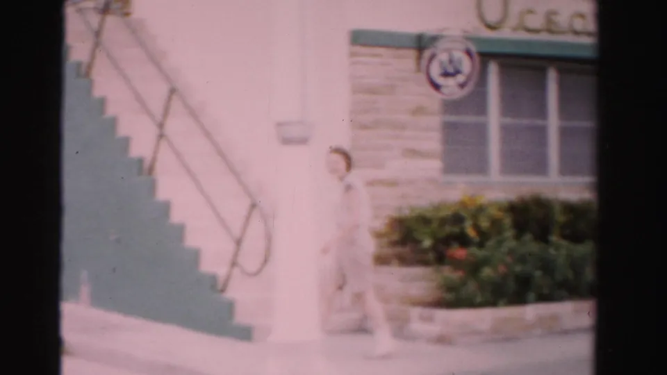 The woman continues along the sidewalk beside exterior stairs at the Ocean Tropicana Motel in Dade County, Florida.