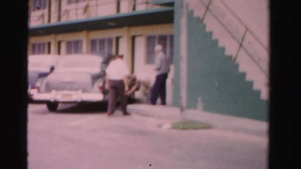 Adults appear near a parked car outside a green-and-white Dade County motel, with other 1950s cars nearby.