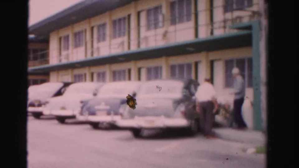 A row of 1950s cars lines the motel parking area while adults stand near one vehicle in Dade County, Florida.